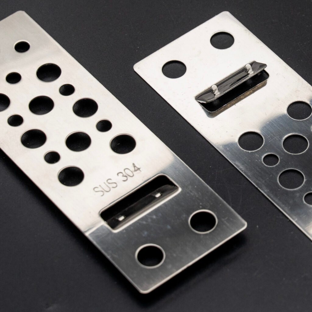 SUS 304 stainless steel porcelain panel cladding clips with multi-hole pattern and barbed locking tab — three pieces on black background