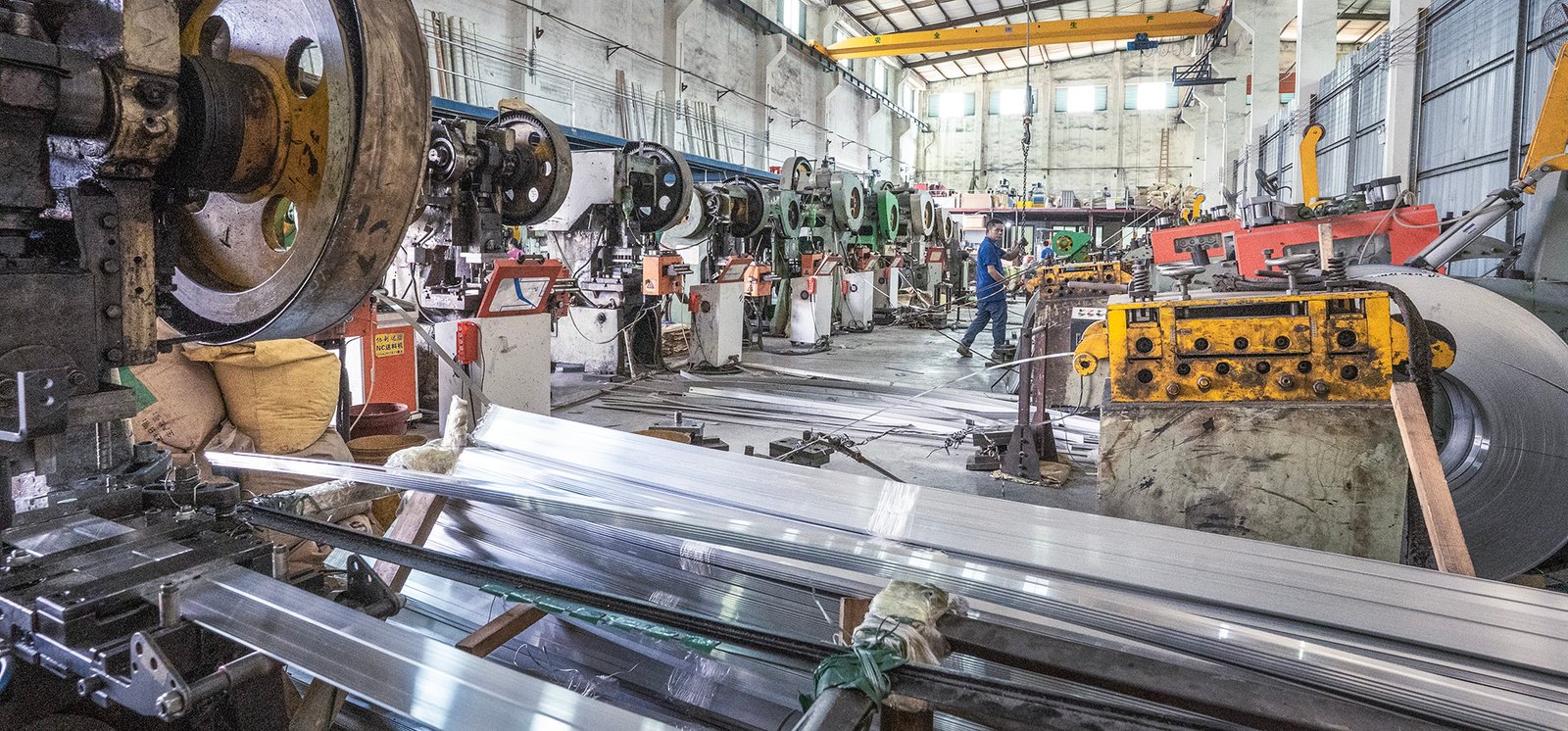 Metal stamping workshop — multiple punch presses in operation with aluminum profiles and coiled metal strip raw materials